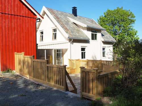 Holiday house, Kårstua, Austrått agrotourism, in the foreground a stone laid patio, in the background a white wooden house, red barn to the left