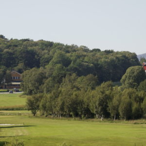 Austrått golfbane, Austrått Agroturisme, en del av en golfbane sees i forgrunnen, skog og en gård i bakgrunnen