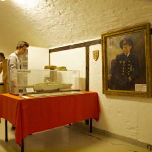 Austrått fort, Fosen krigshistoriske samlinger, Austrått agroturisme, en person ser på en modell av slagskipet Gneisenau, på veggen henger et maleri av tidligere kommandør på Austrått fort