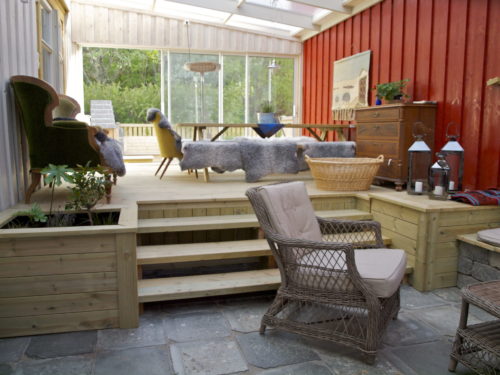 Austrått agrotourism, Kårstua, wintergarden with a transparent plastic roof, slate floor, stairs up to a dining table, sliding doors in the background, red wall to the right, white wall to the left.