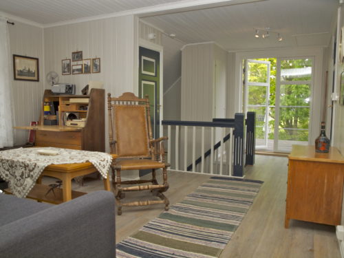 Holiday house, Austrått agrotourism, Kårstua, loft living room, light grey walls, dark grey sofa,a brown america rocking chair in the middle of the picture, an open glass door in the background