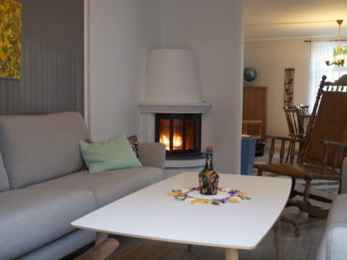 Feriehus, Austrått agroturisme, Kårstua, stue med hjørnepeis, mørk grå panel og hvit brannmur, lys grå sofa og hvitt bord