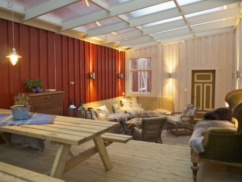 Austrått agrotourismus, Kårstua, wintergarten mit transparentem Kunststoffdach, esstisch mit bänken auf der linken Seite, rote wand nach links, weiße wand auf der rückseite, wandbeleuchtung, sitzbereich in der ecke auf der rückseite