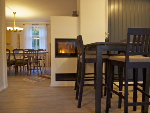 Feriehus, Austrått agroturisme, Kårstua, kjøkkenbord med barkrakker til høyre, i bakgrunnen til venstre et spisebord, i midten en hvit peisovn