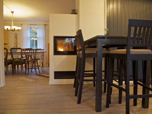 Ferienhaus, Austrått agrotourismus, Kårstua, rechts küchentisch mit barhockern t, im hintergrund links ein esstisch, in der mitte ein weisse kamin